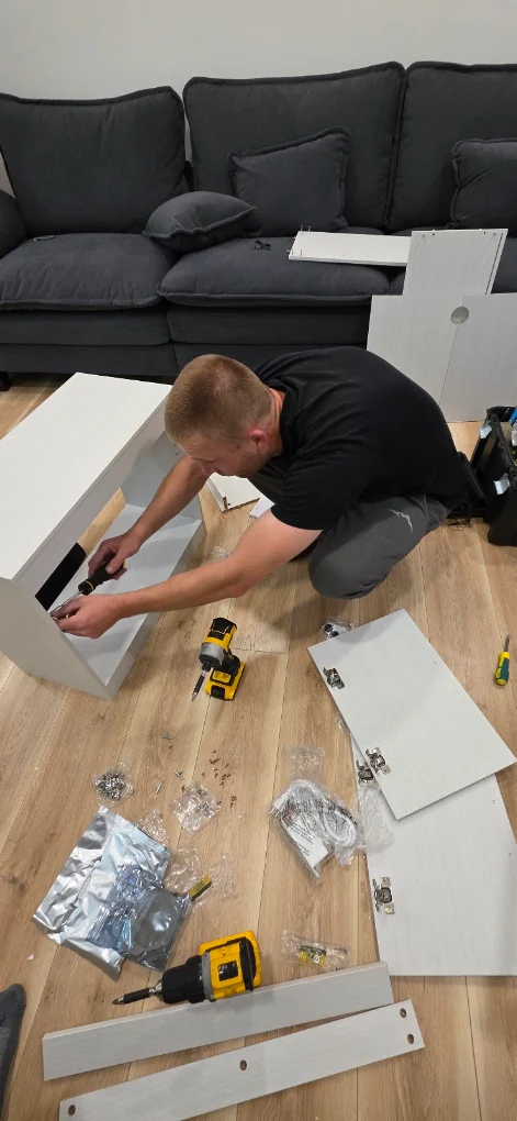 Dmitry assembling a white flat-pack cabinet in a Calgary living room, hinges and hardware laid out ready