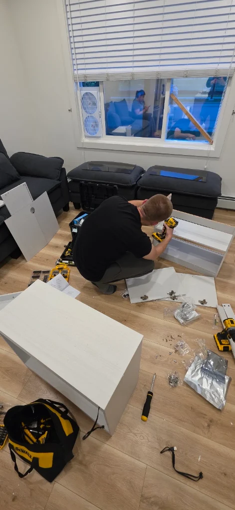 Dmitry building a white flat-pack drawer unit on site in Calgary, panels and fittings set out on the floor